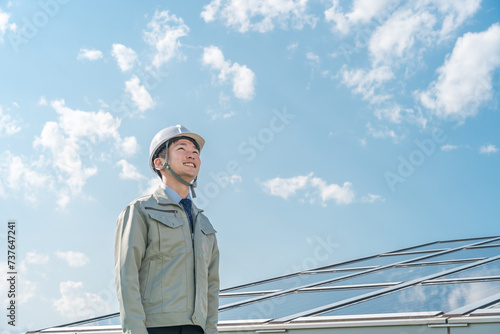 Obraz na płótnie 太陽光発電・ソーラーパネルの前に立つ電力会社・電気工事業者の作業着姿の技術者（クリーンエネルギー） 
