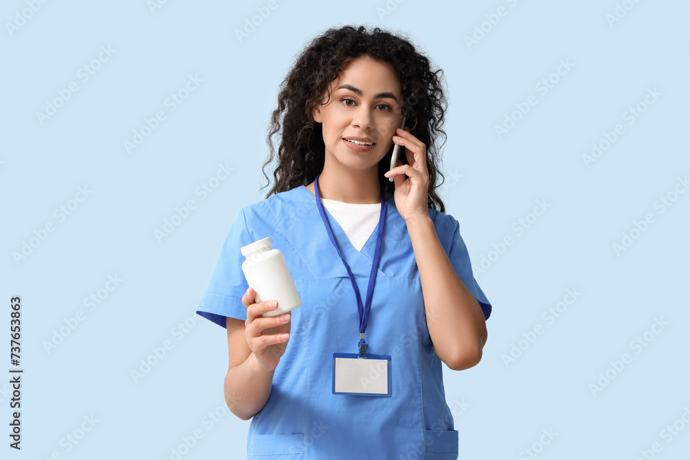 Female African-American medical intern with pill bottle talking by mobile phone on blue background Female African-American medical intern with pill bottle talking by mobile phone on blue background