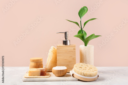 Composition with soap, sea salt and brush on table near pink wall. Bath accessories
