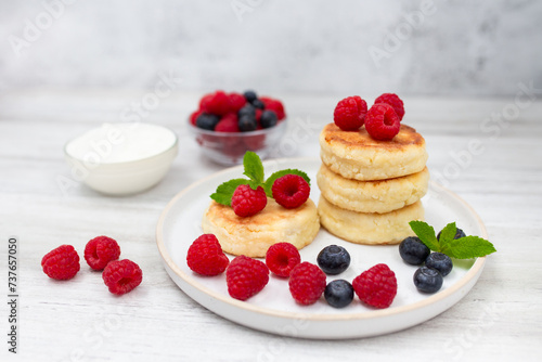 Cottage cheese pancake or syrniki with fresh raspberries and blueberry on white wooden table. Sweet breakfast or lunch, tasty dessert. 
