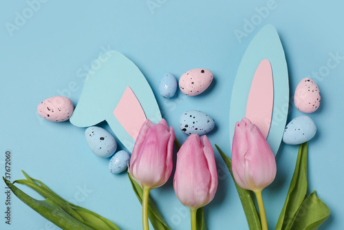 Tulips with Easter eggs and bunny ears on blue background