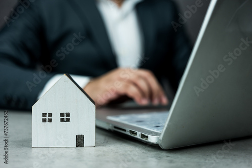 Businessman working on a computer with a white wooden house model in front of them. Smart home technology concept. Concept of rent, search and purchase real estate.