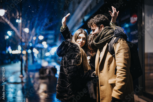 A playful young couple enjoys a snowy evening in the city's glow. They are dressed in cozy winter attire, creating a feeling of warmth and joy despite the chilly weather.