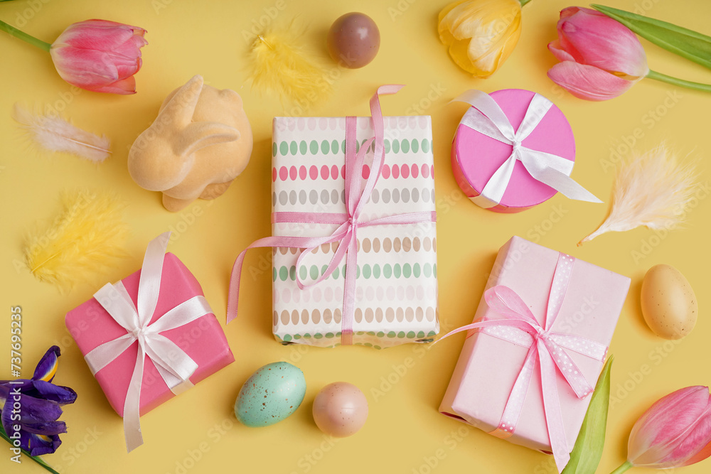Easter gifts, painted eggs, tulips and bunny figure on yellow background
