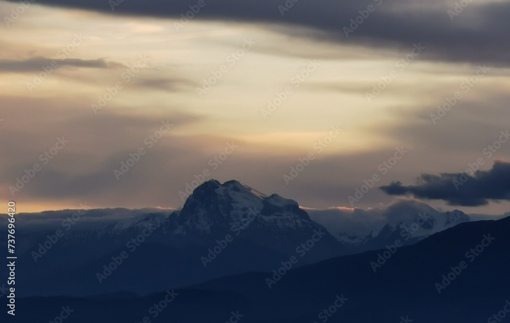Le cime delle montagne innevate al tramonto nel cielo plumbeo invernale