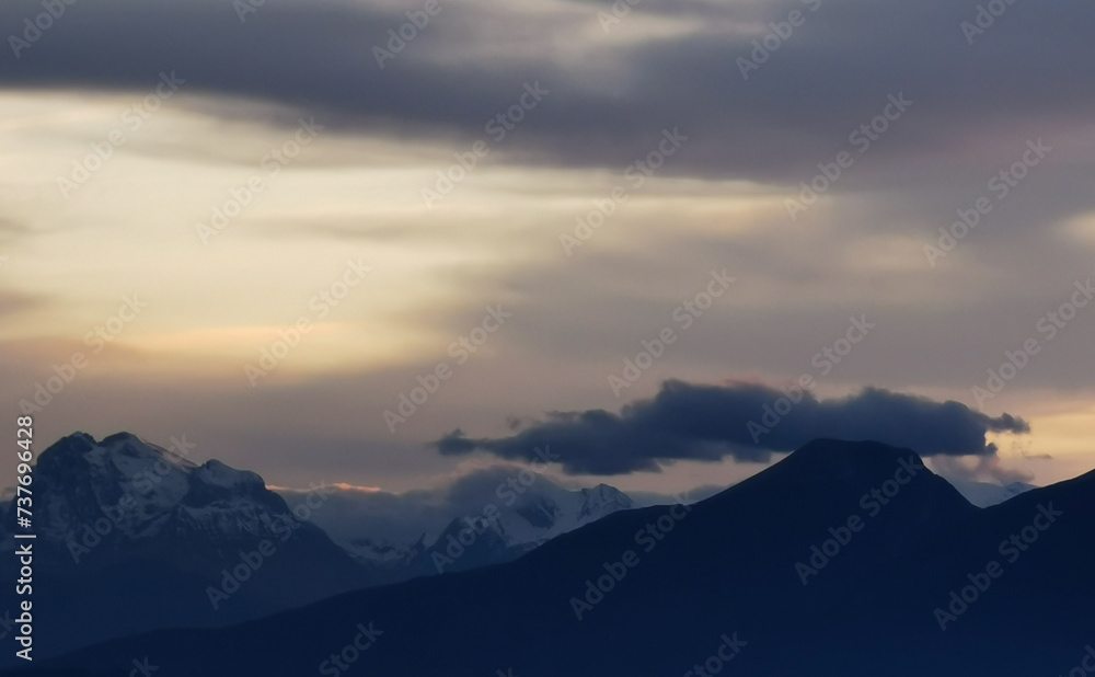 Le cime delle montagne innevate al tramonto nel cielo plumbeo invernale
