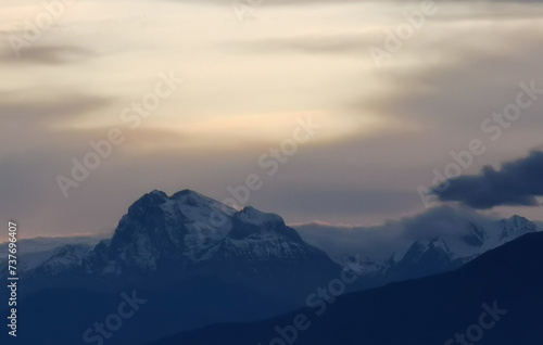 Le cime delle montagne innevate al tramonto nel cielo plumbeo invernale © GjGj
