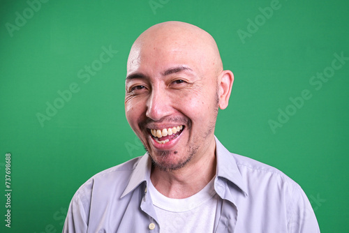 Portrait of Asian bald man smiling over green background © Gatot