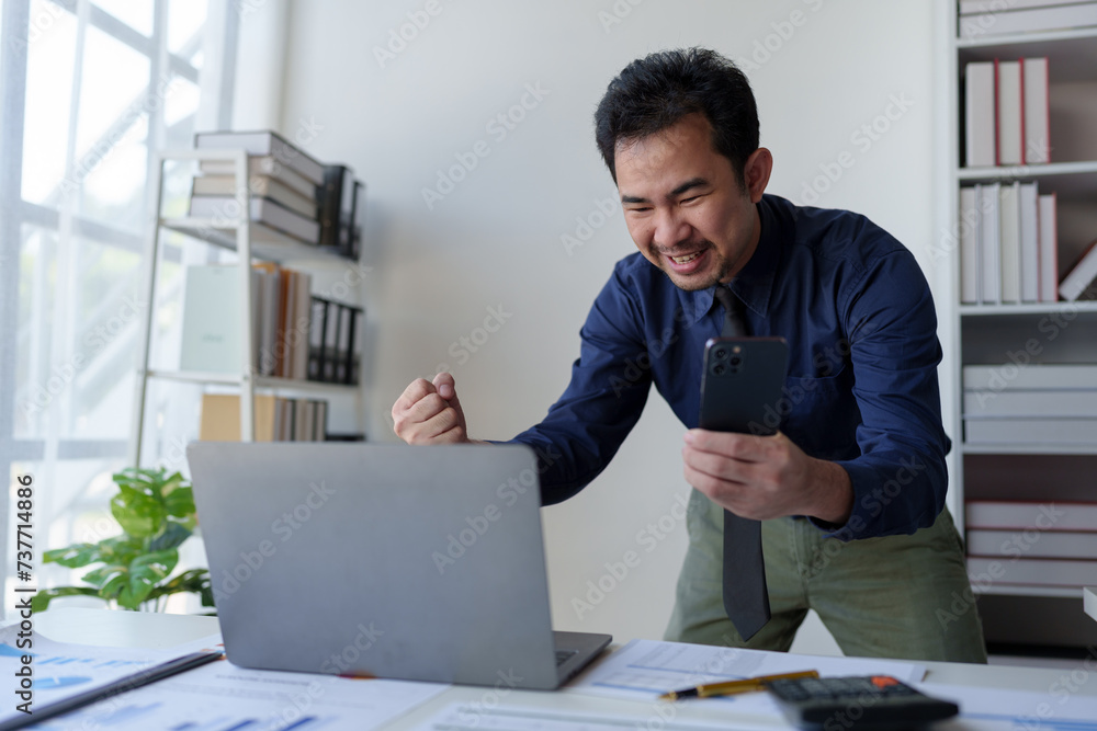 Businessman holding smartphone showing happy expression while receiving confirmation email on laptop Response to investment in financial business Earn bonuses based on successful business goals. Businessman holding smartphone showing happy expression while receiving confirmation email on laptop Response to investment in financial business Earn bonuses based on successful business goals.