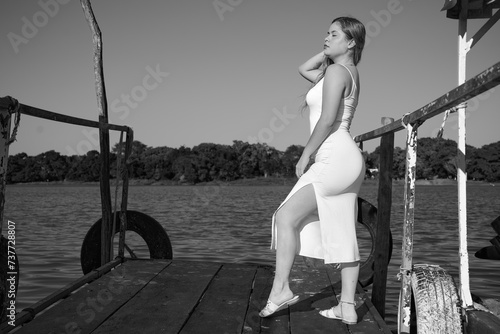 black dress, Latina with blue sky, and posing next to the lake, full body, face, posing at the dock, nice figure in black and white
