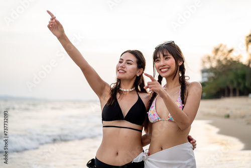 Asian two women friends walking on the beach during summer together.