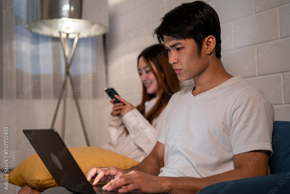 Asian young man overworking on laptop with his wife beside at night. Asian young man overworking on laptop with his wife beside at night.