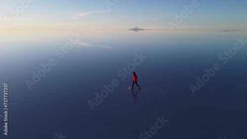 Woman walks on reflective surface of Uyuni Salt Flat, Bolivia aerial photo
