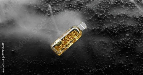 Bottle of 24k Gold bottle on black rock background is surrounded by a milky white haze photo