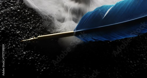 Symbolic blue writing feather sits on black rocks as mythical smoke surrounds it photo
