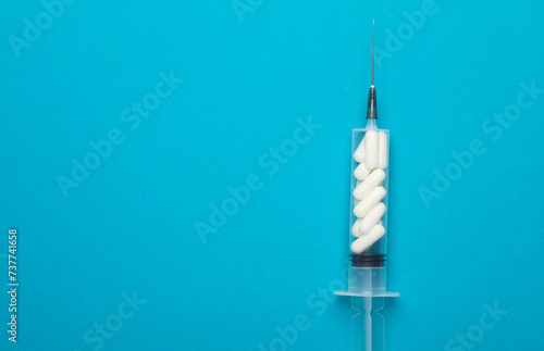 The syringe is filled with pills on a blue background. Healthcare and medicine concept