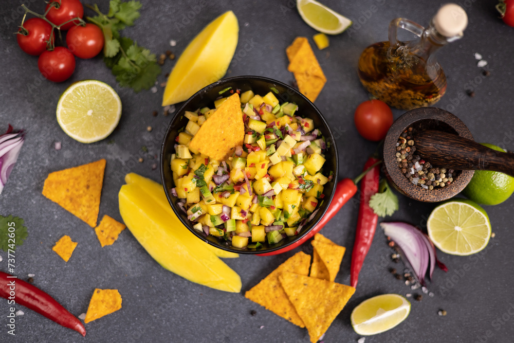 Freshly made mango salsa in a black ceramic bowl, nacho chips and ingredients