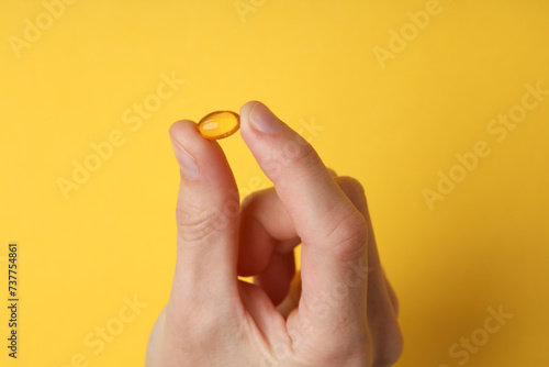 Hand holding fish oil capsule on yellow background