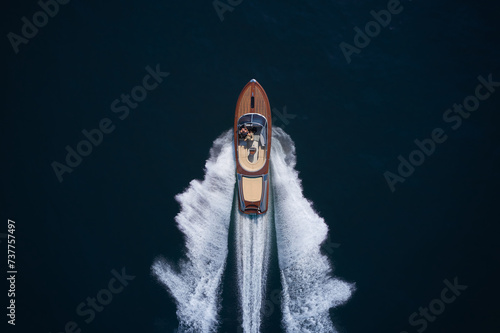 Classic Italian wooden boat fast moving aerial view. Luxurious wooden boat fast movement on dark water. A large modern high-speed wooden luxury boat. Top view of a wooden powerful motor boat.