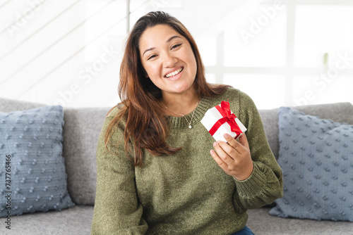 Young biracial woman holding a gift box at home on a video call, with copy space