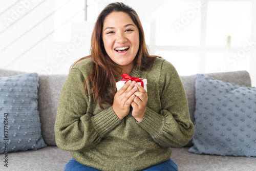 Young Biracial woman holding a small gift box at home on a video call, with copy space