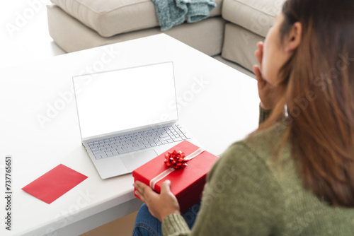 Young biracial woman at home with a gift on a video call, with copy space