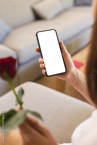 A young woman holds a smartphone and a red rose, on a video call with copy space
