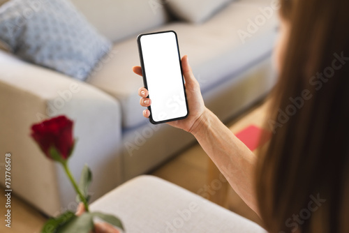A young Caucasian woman is holding a smartphone with a blank screen, with copy space, and a red rose