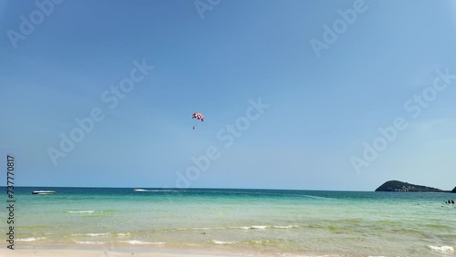 Scenic tropical beach with clear blue skies, a parasailer in the distance, and speedboats near the shore, perfect for travel and summer holiday themes photo