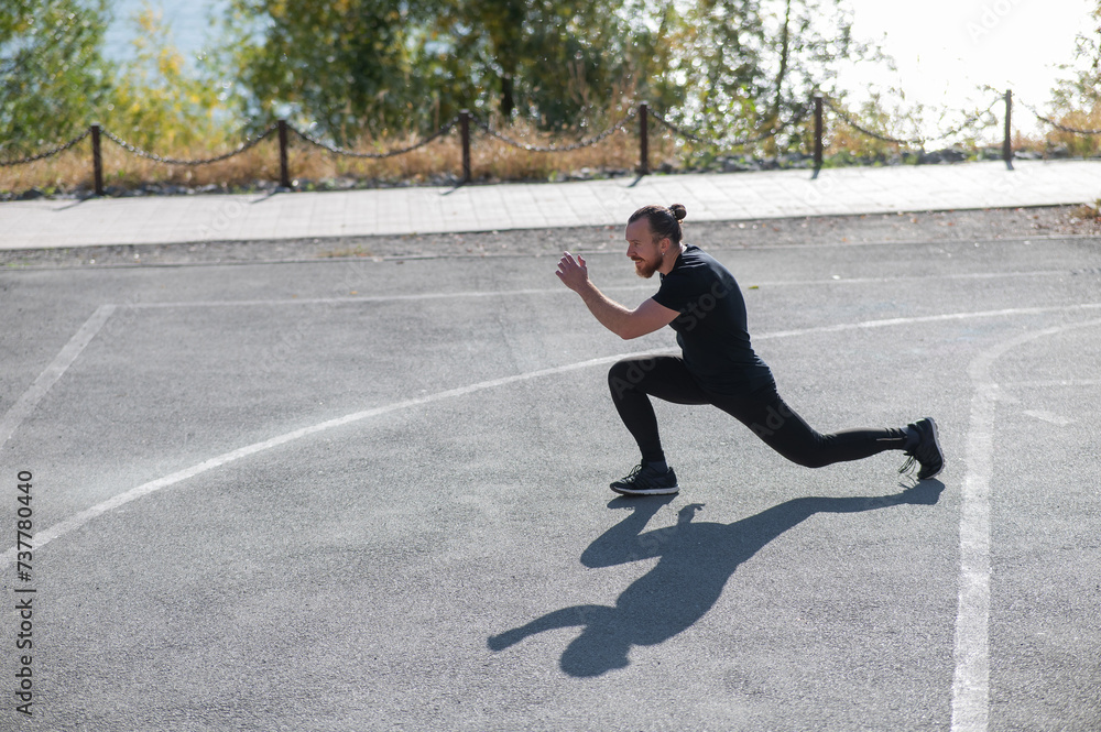 Fototapeta premium Bearded man with long hair doing lunges on the sports field. 