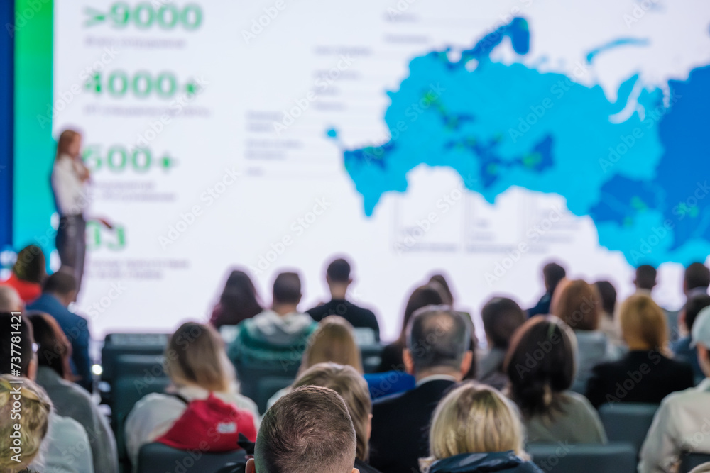 Speaker giving a presentation at a business conference, with attendees listening to global growth strategies. Speaker giving a presentation at a business conference, with attendees listening to global growth strategies.