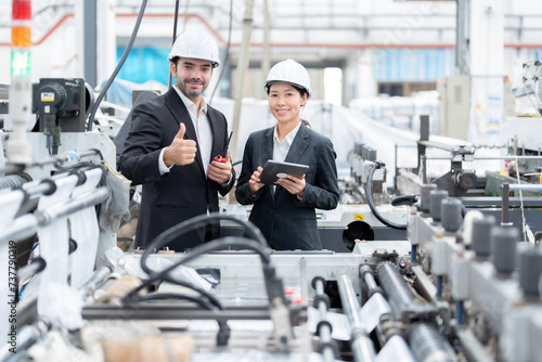 senior official Asian woman and European male architectural engineer thumbs up like symbol Work in the plastics and steel industry, wear a suit, safety helmet, use a laptop and walkie-talkie.