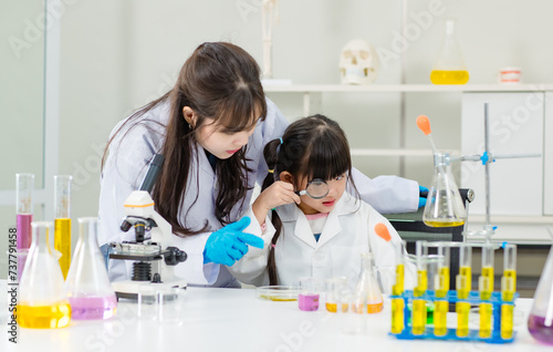 Asian woman scientist and little girl looking through magnifying glass making science experiments tests have microscope at chemical laboratory study room. Education concept learning for kids