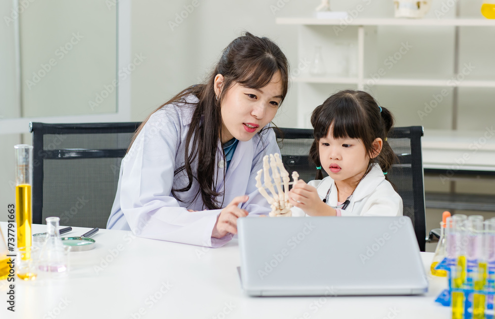 Asian woman doctor physiotherapist explains human fake body skeleton model on a table to little children girl at laboratory study room. Education anatomical human concept learning for kids. Asian woman doctor physiotherapist explains human fake body skeleton model on a table to little children girl at laboratory study room. Education anatomical human concept learning for kids.