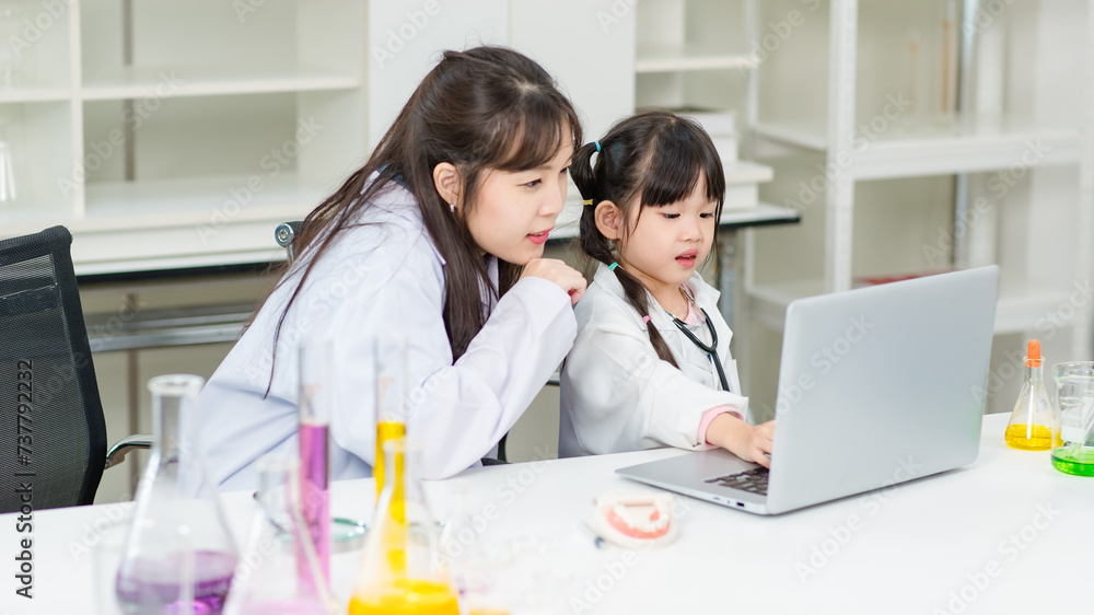 Asian woman teacher and little children girl reading laptop computer for data learning science at chemical laboratory study room. Education research and development concept learning for kids. Asian woman teacher and little children girl reading laptop computer for data learning science at chemical laboratory study room. Education research and development concept learning for kids.