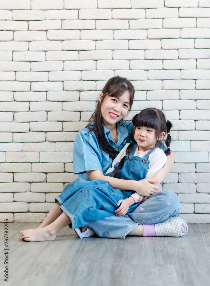 Happy asian beautiful young mother and cute daughter little girl smiling posing hugging on white brick wall background studio portrait Mother's Day love family parenthood childhood concept. Happy asian beautiful young mother and cute daughter little girl smiling posing hugging on white brick wall background studio portrait Mother's Day love family parenthood childhood concept.