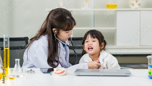 Asian woman doctor and cheerful little girl applying medical stethoscope at doctor appointments in laboratory lab. Education healthcare, medicine childrens hospital concept learning for kids
