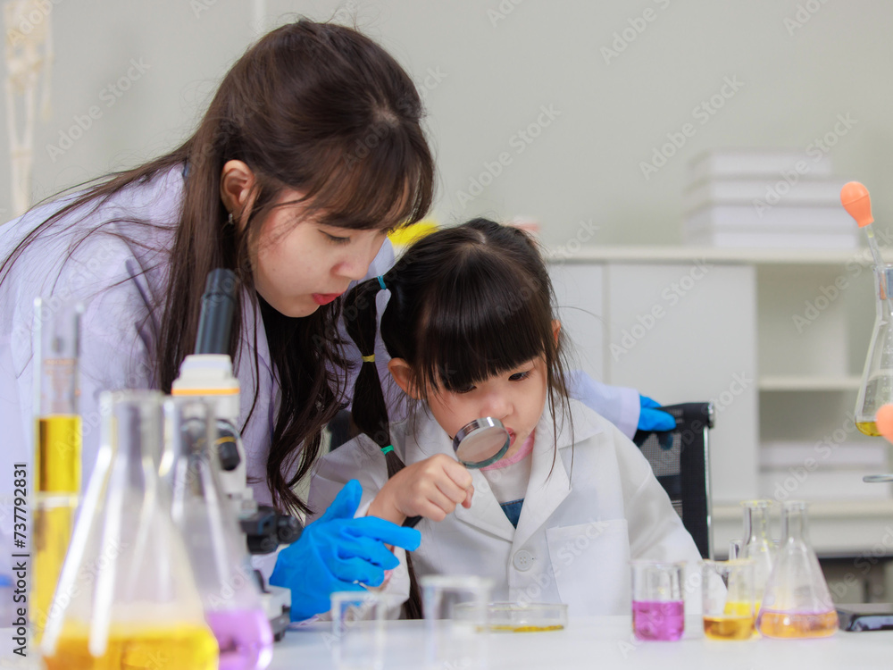 Asian woman scientist and little girl looking through magnifying glass making science experiments tests have microscope at chemical laboratory study room. Education concept learning for kids Asian woman scientist and little girl looking through magnifying glass making science experiments tests have microscope at chemical laboratory study room. Education concept learning for kids