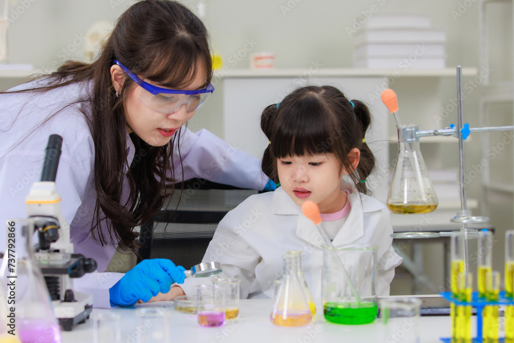Asian woman scientist and little girl looking through magnifying glass making science experiments tests have microscope at chemical laboratory study room. Education concept learning for kids Asian woman scientist and little girl looking through magnifying glass making science experiments tests have microscope at chemical laboratory study room. Education concept learning for kids