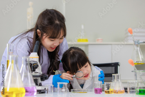 Asian woman scientist and little girl looking through magnifying glass making science experiments tests have microscope at chemical laboratory study room. Education concept learning for kids