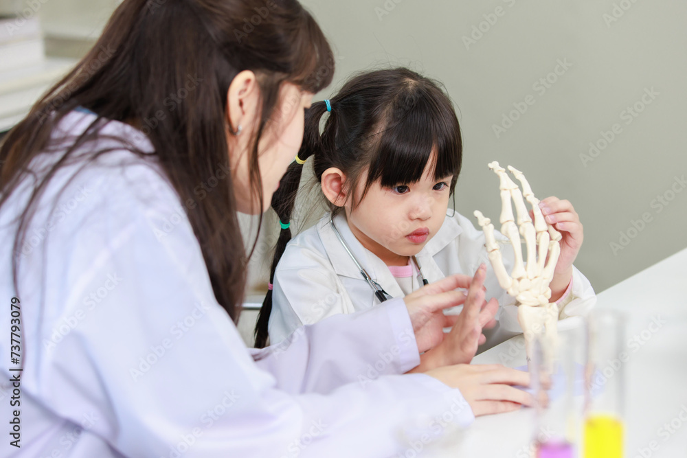 Asian woman doctor physiotherapist explains human fake body skeleton model on a table to little children girl at laboratory study room. Education anatomical human concept learning for kids. Asian woman doctor physiotherapist explains human fake body skeleton model on a table to little children girl at laboratory study room. Education anatomical human concept learning for kids.