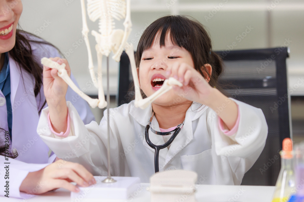 Asian woman doctor physiotherapist explains human fake skeleton hand model on a table to little cute children girl at laboratory study room. Education anatomical human concept learning for kids. Asian woman doctor physiotherapist explains human fake skeleton hand model on a table to little cute children girl at laboratory study room. Education anatomical human concept learning for kids.