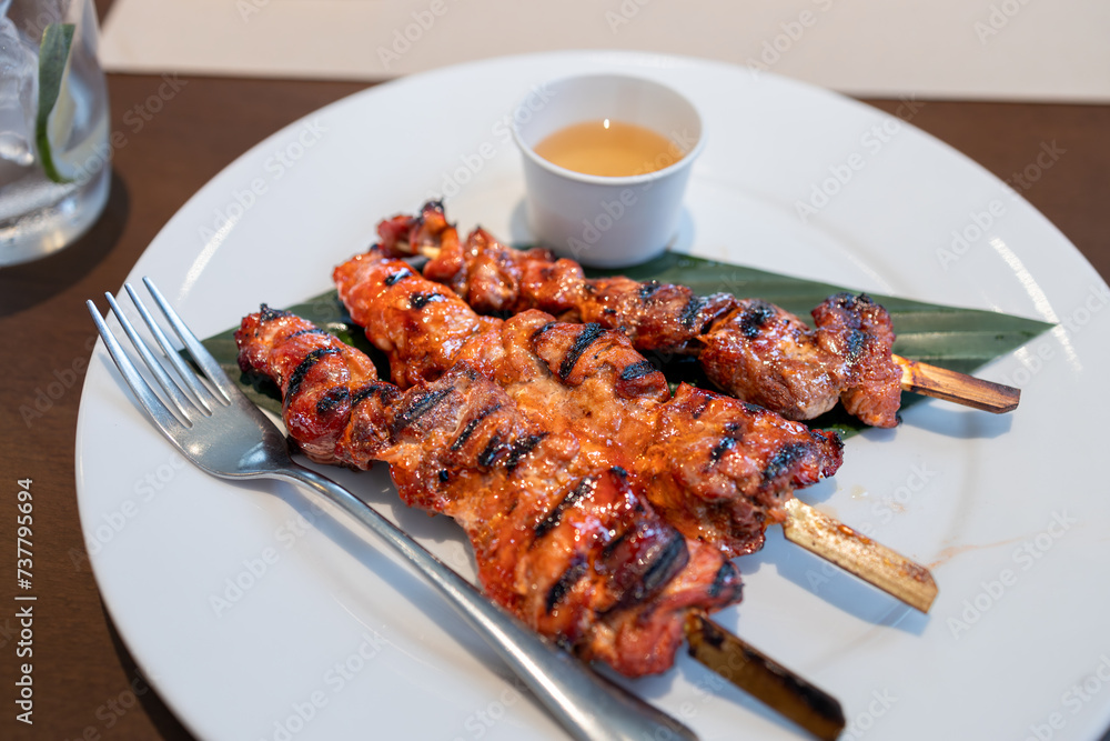 Grilled pork ribs with sauce on white plate and wooden table, Philippines
