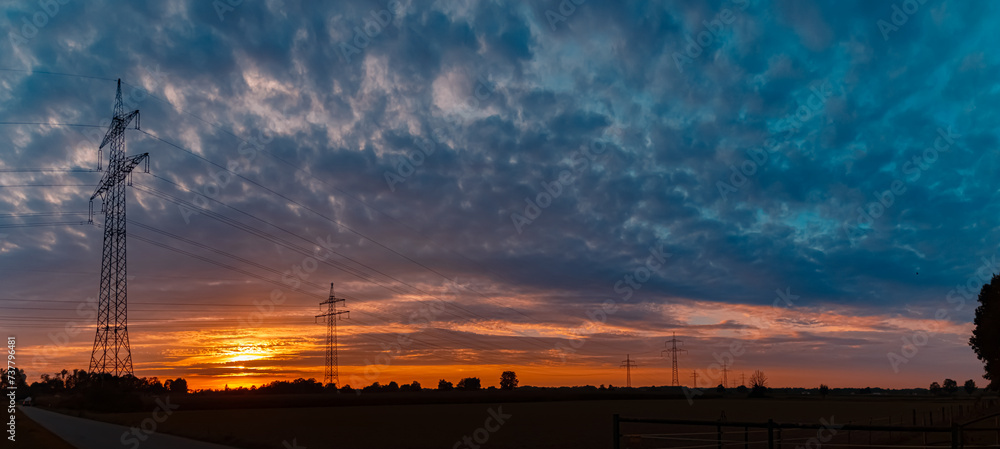 Sunset with a dramatic sky and overland high voltage lines near Tabertshausen, Bavaria, Germany