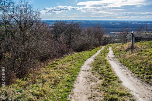 Unpaved road with grass overlooking the lowlands. There are bushes on the left side.