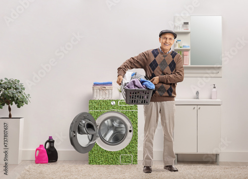 Elderly man holding a laundry basket full of clothes inside a bathroom with a power efficient washing machine