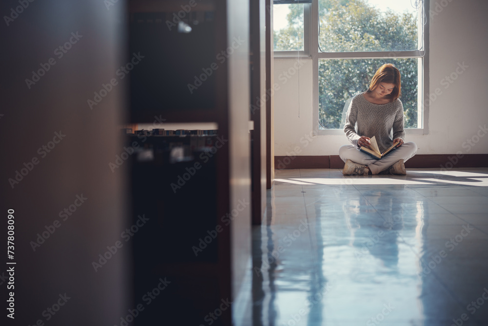 Young asian female college student sitting on floor in library, reading book. Young asian female college student sitting on floor in library, reading book.
