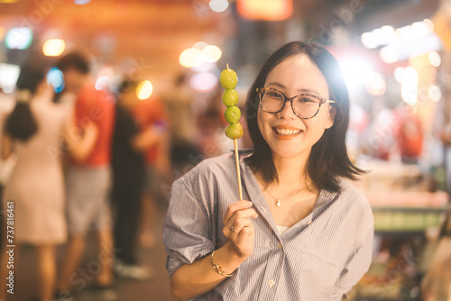 Young adult asian foodie woman eating chinese dessert Tanghulu at china town street food photo