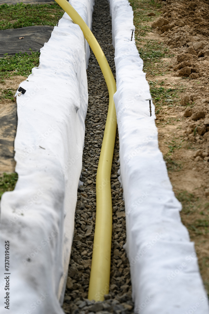 Yellow corrugated pipe with perforation in a trench with crushed stone and geotextile. Drainage works for the removal of ground water. Yellow corrugated pipe with perforation in a trench with crushed stone and geotextile. Drainage works for the removal of ground water.