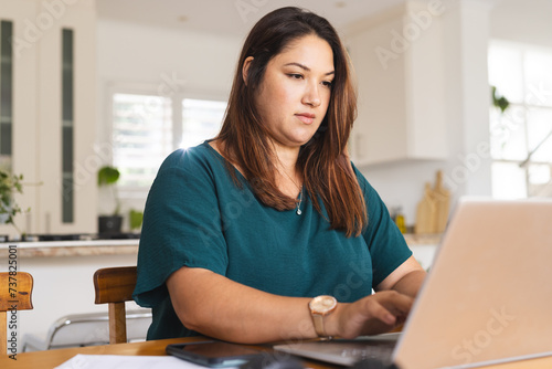 Young plus size biracial woman works diligently on her laptop at home, unaltered photo